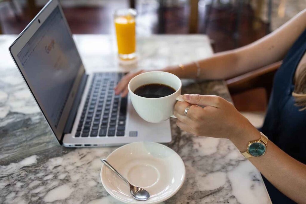 Woman holding a cup of coffee while tapping on a laptop keyboard